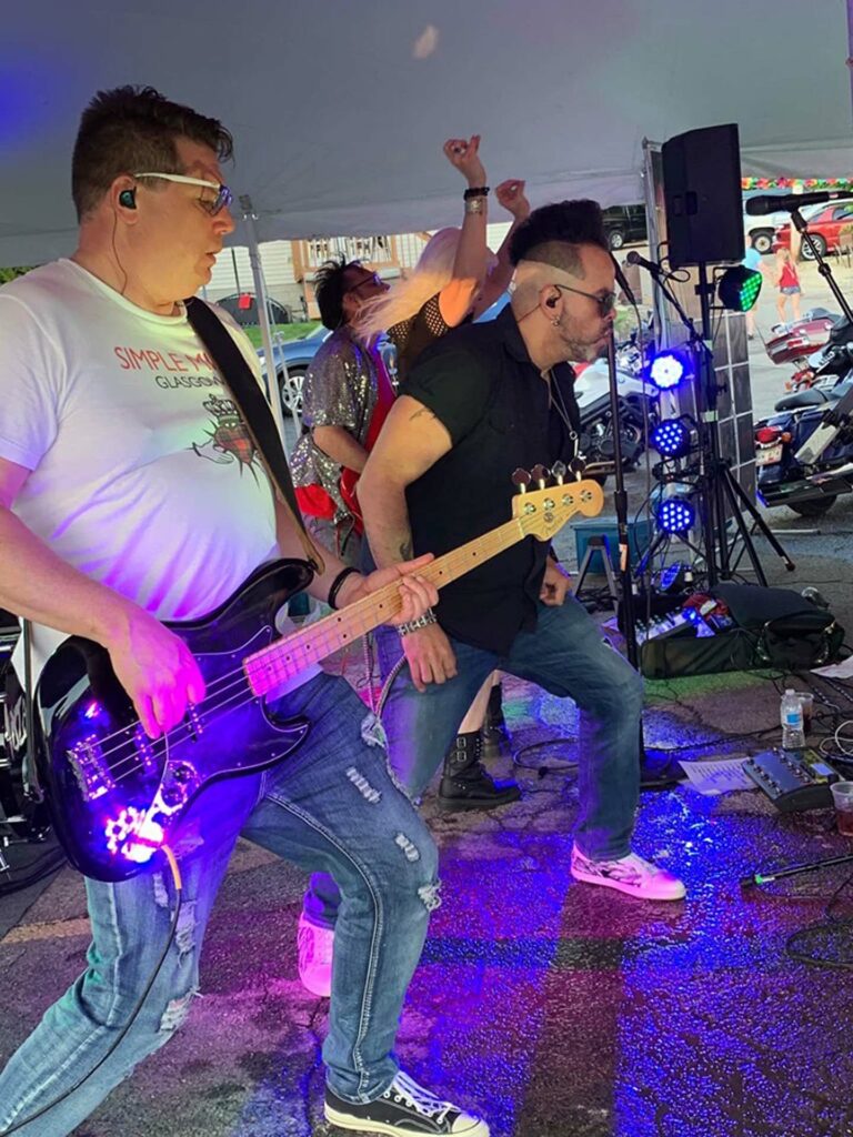 Band members dancing with buy playing bass under a tent at an outside festival