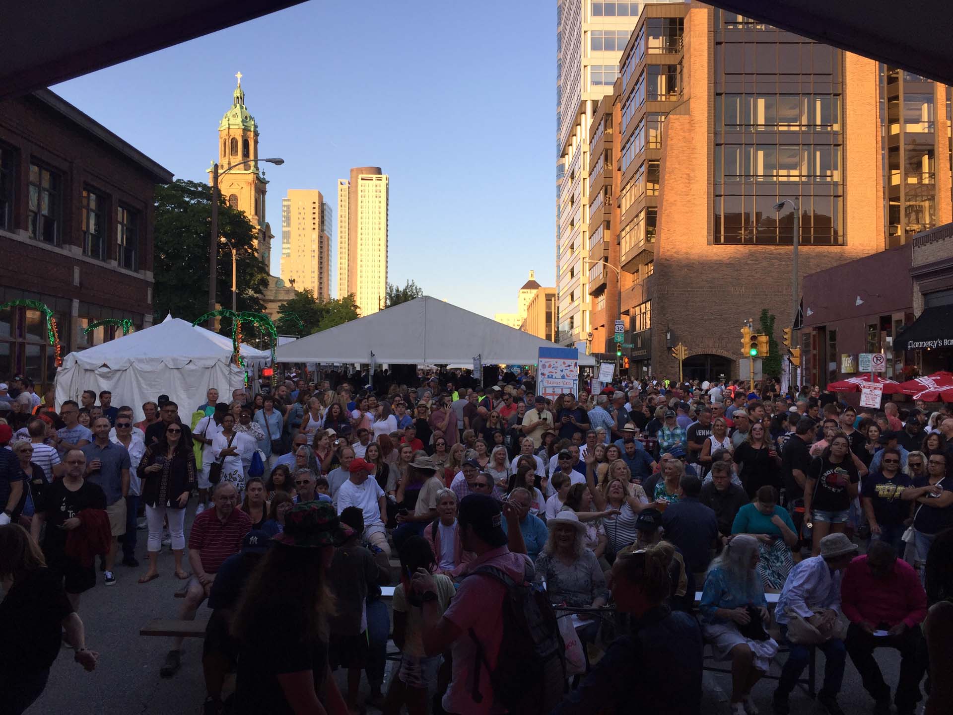 crowd on street surrounded by tall buildings at an outside festival listening to band